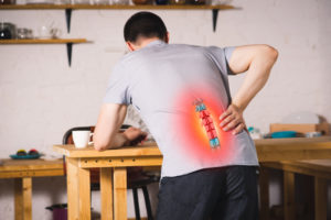A man leaning over a table in pain holding his lower back