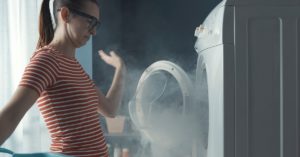 A woman standing inn from of an open washing machine with smoke pouring out.