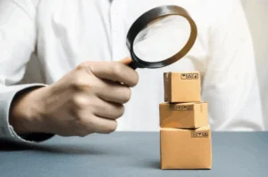 A man holding a magnifying glass and looking at small boxes. An attorney can explain if you can get compensation for injuries caused by a defective product.