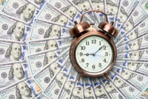 Top-down view of a clock sitting face-up on top of a pile of money to symbolize the question of how long it takes to settle a truck accident case.
