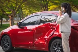 A driver calls for help while standing near her damaged car. Fault in a car accident depends on evidence showing how the crash occurred.