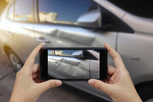 A motorist takes a picture of vehicle damage after a crash using a cell phone. The best way to document a car accident is to gather clear photos, basic facts, and witness details as soon as it is safe, before vehicles move and memories fade.