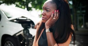 A woman in front of her car after a collision, wondering if a car crash lawyer can settle her lawsuit.
