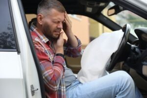 A man in a car clutching his head after an accident. Learn about whether it’s crucial to seek medical attention after a truck accident.