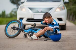 Child who is riding a bicycle, has been hit by a car, and is dealing with an injury, with their parent nearby, wondering what types of accidents child injury lawyers handle. 